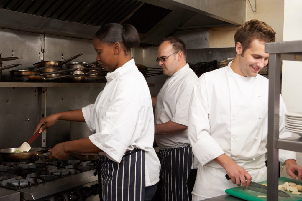 Tre personer arbetar tillsammans i ett professionellt restaurangkök.